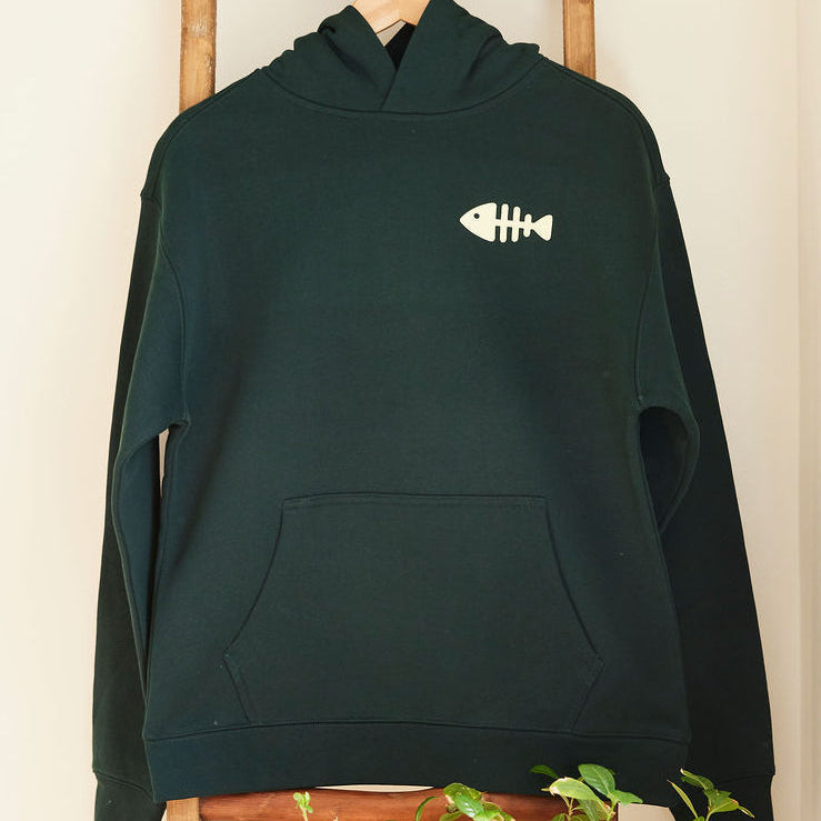 Green hoodie with a fish design on a wooden ladder against a white wall.